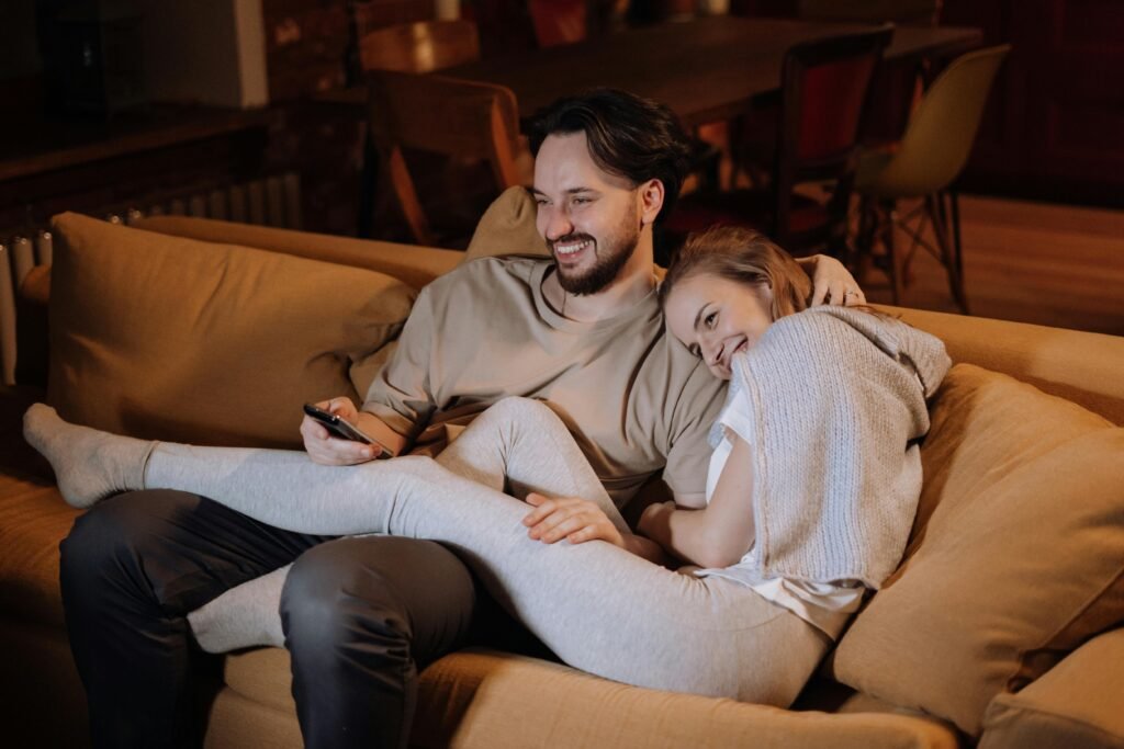 Happy couple enjoying a cozy evening at home on the couch, watching TV and hugging.
